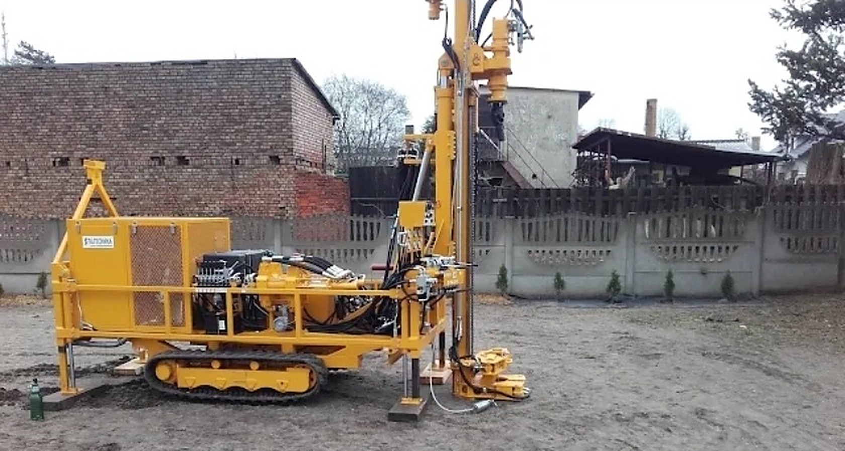 Żółta wiertnica gąsienicowa z masztem wiertniczym, ustawiona na placu roboczym